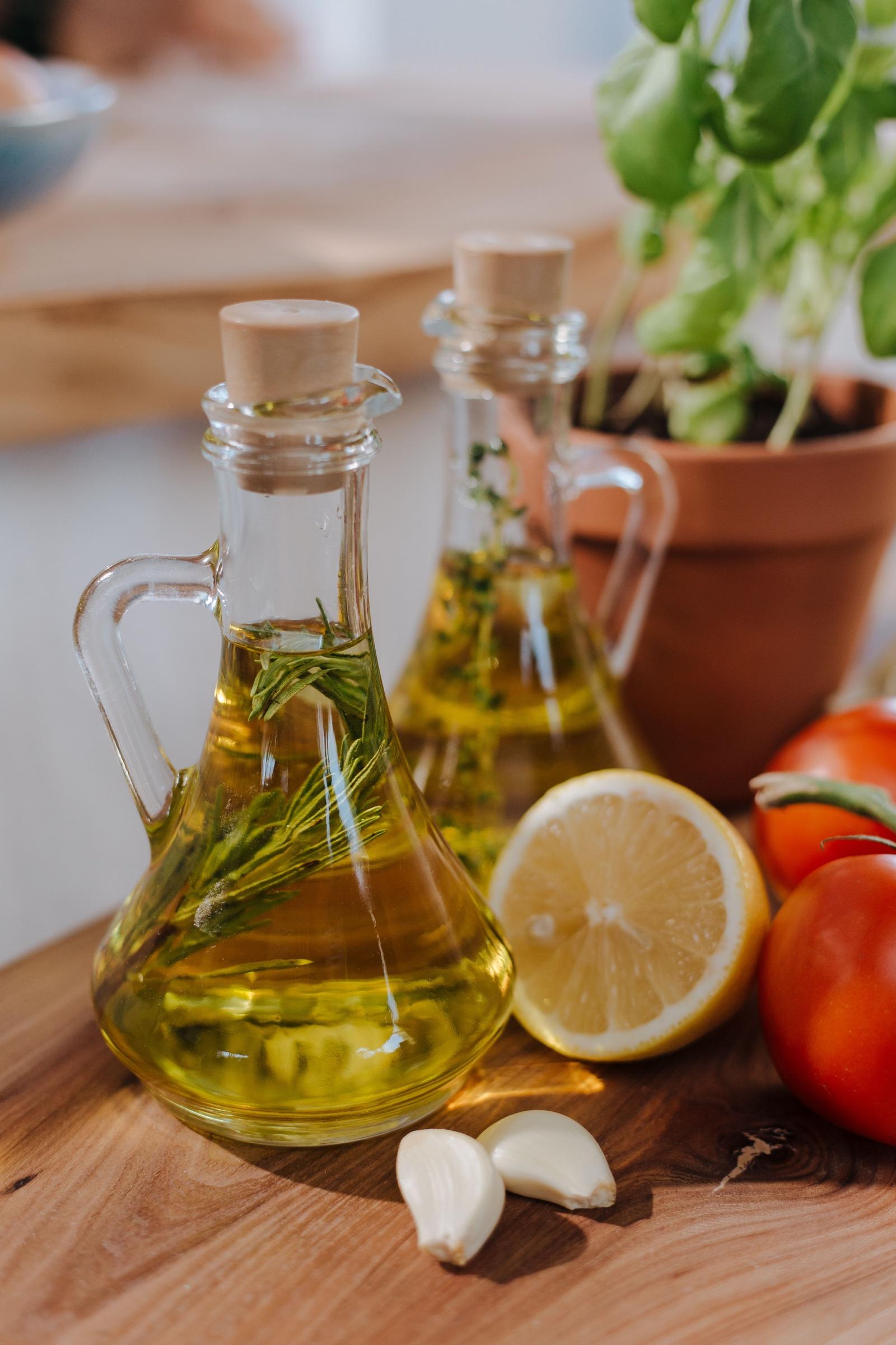 Olive oil infused with herbs beside lemon, tomatoes, garlic, and basil in a warm kitchen.