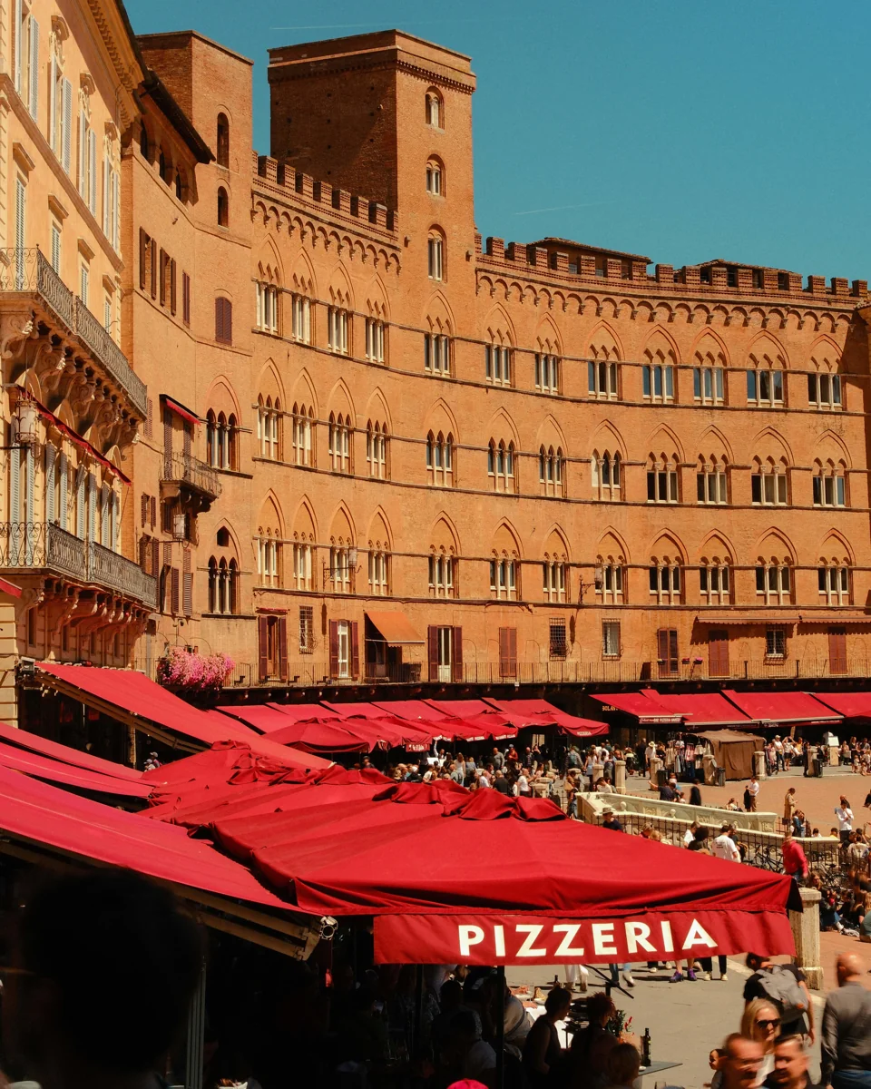 Red café awnings beneath the curved brick façades of Piazza del Campo.