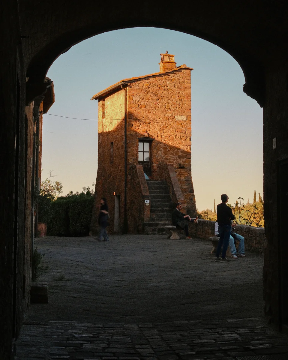 A small brick building and visitors seen through a deep shadowed archway.