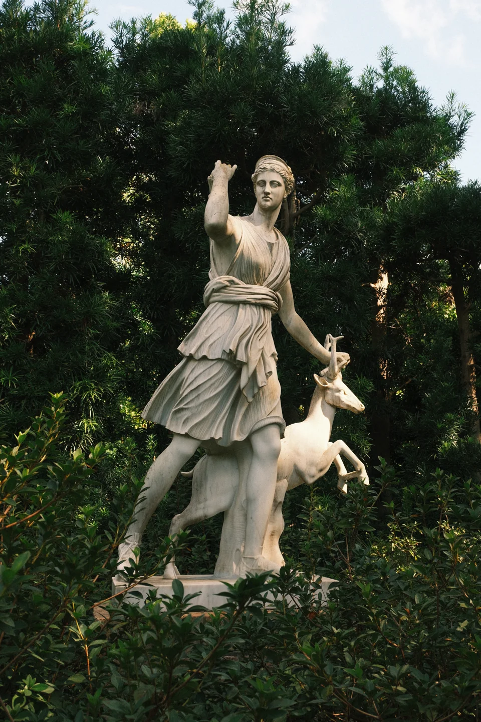 A stone figure with a raised arm and an animal at its side, framed by dark foliage.