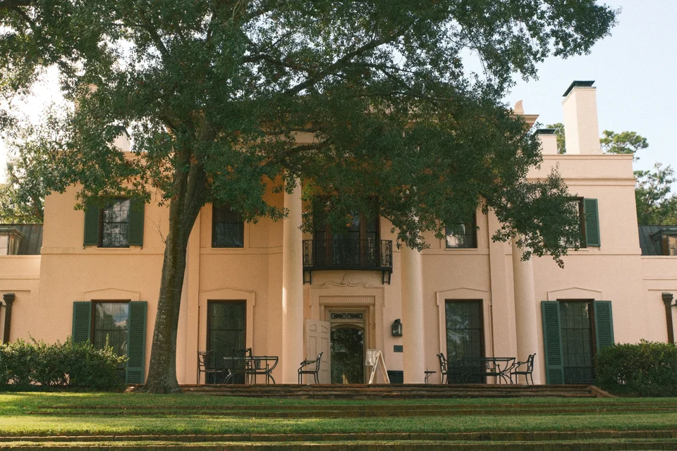 The columned façade of Bayou Bend shaded by a large tree on the lawn.
