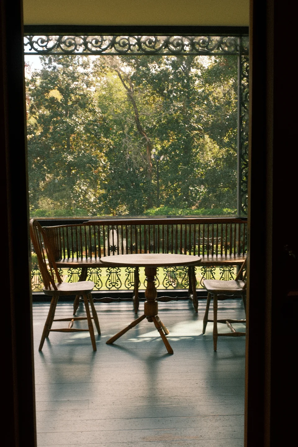 A table and chairs on a shaded porch, seen through a dark doorway toward the trees.