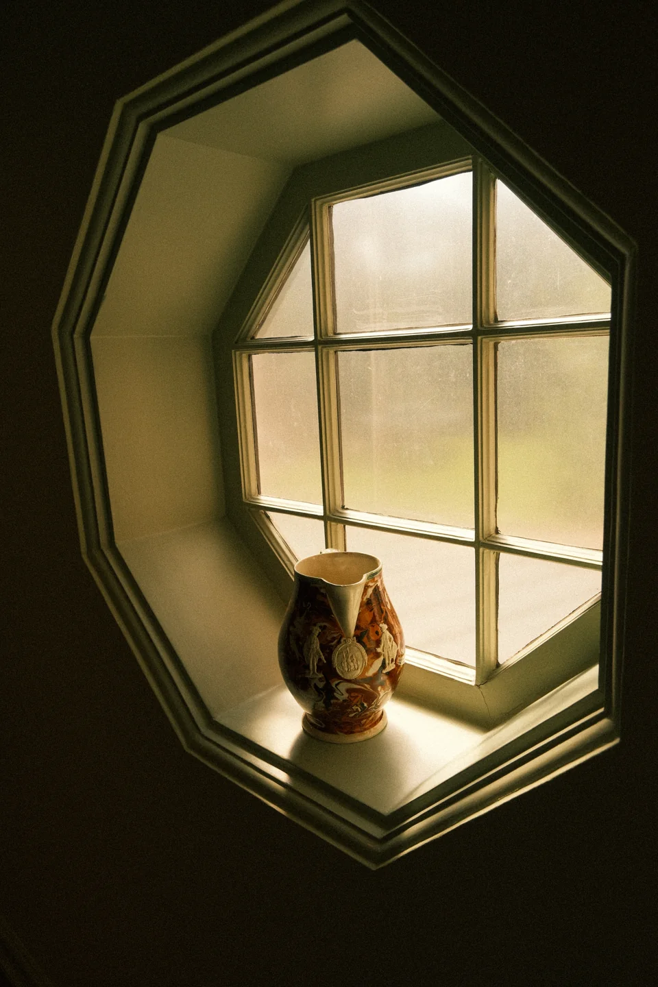 A small decorative vessel on the sill of an octagonal window glowing with soft light.